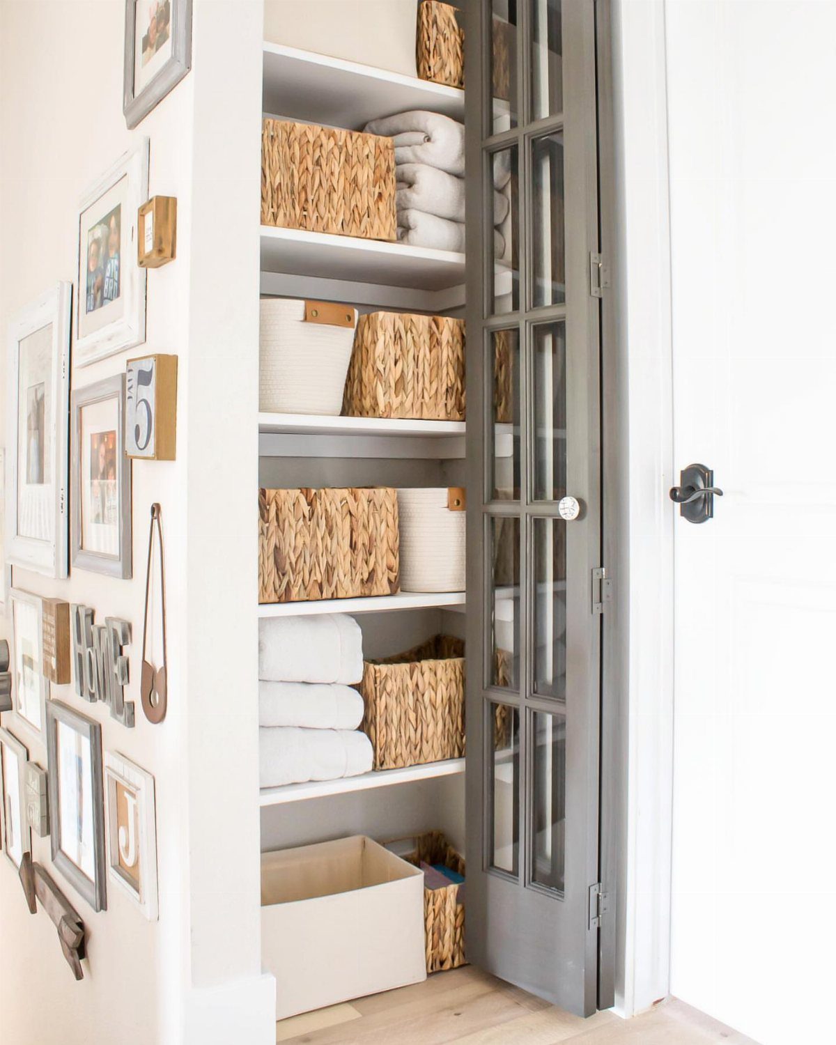 Linen closet with grey glass doors containing white towels and wicker storage baskets.