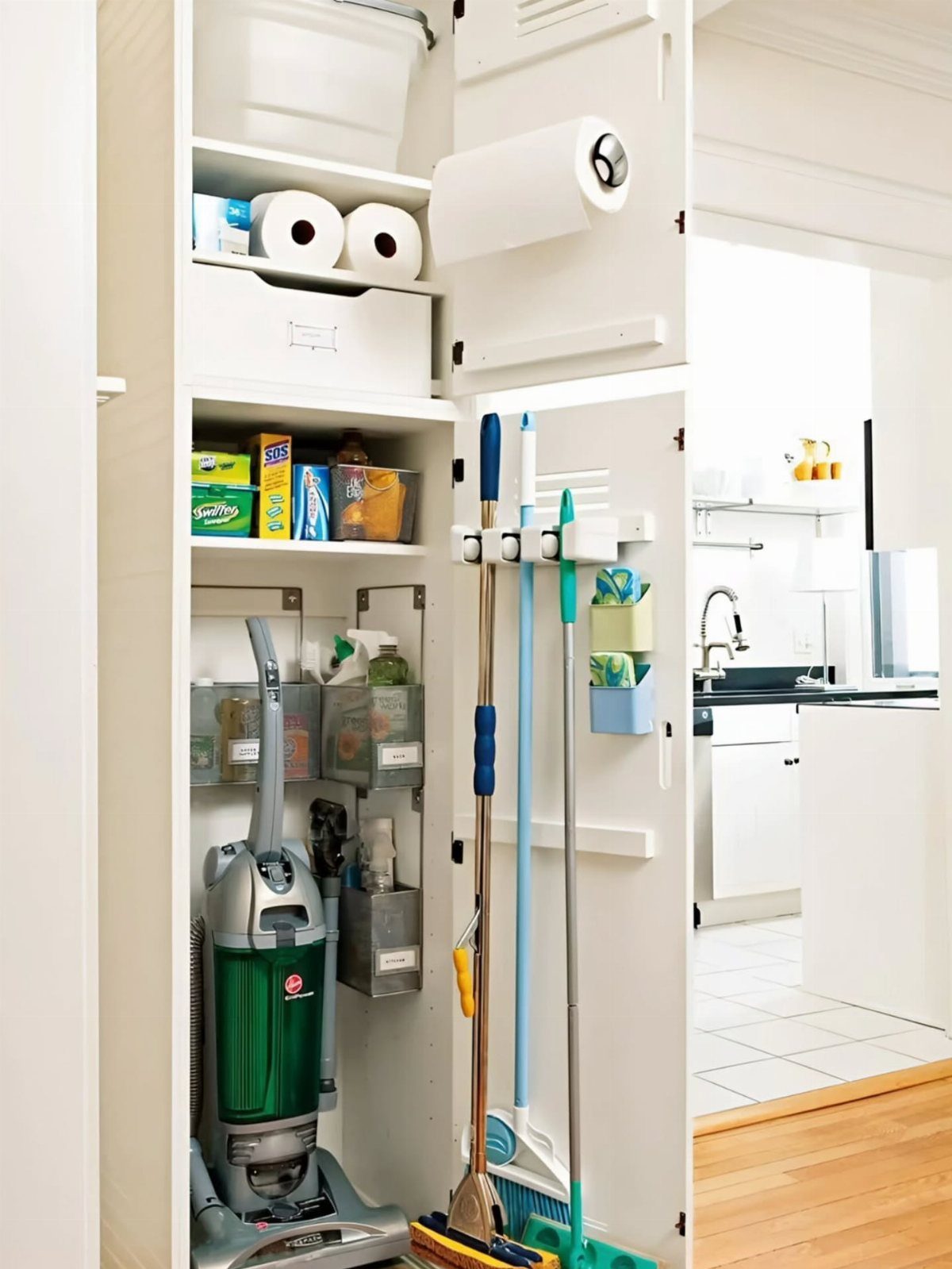 White utility closet with vacuum, brooms, and cleaning supplies on organized shelves.