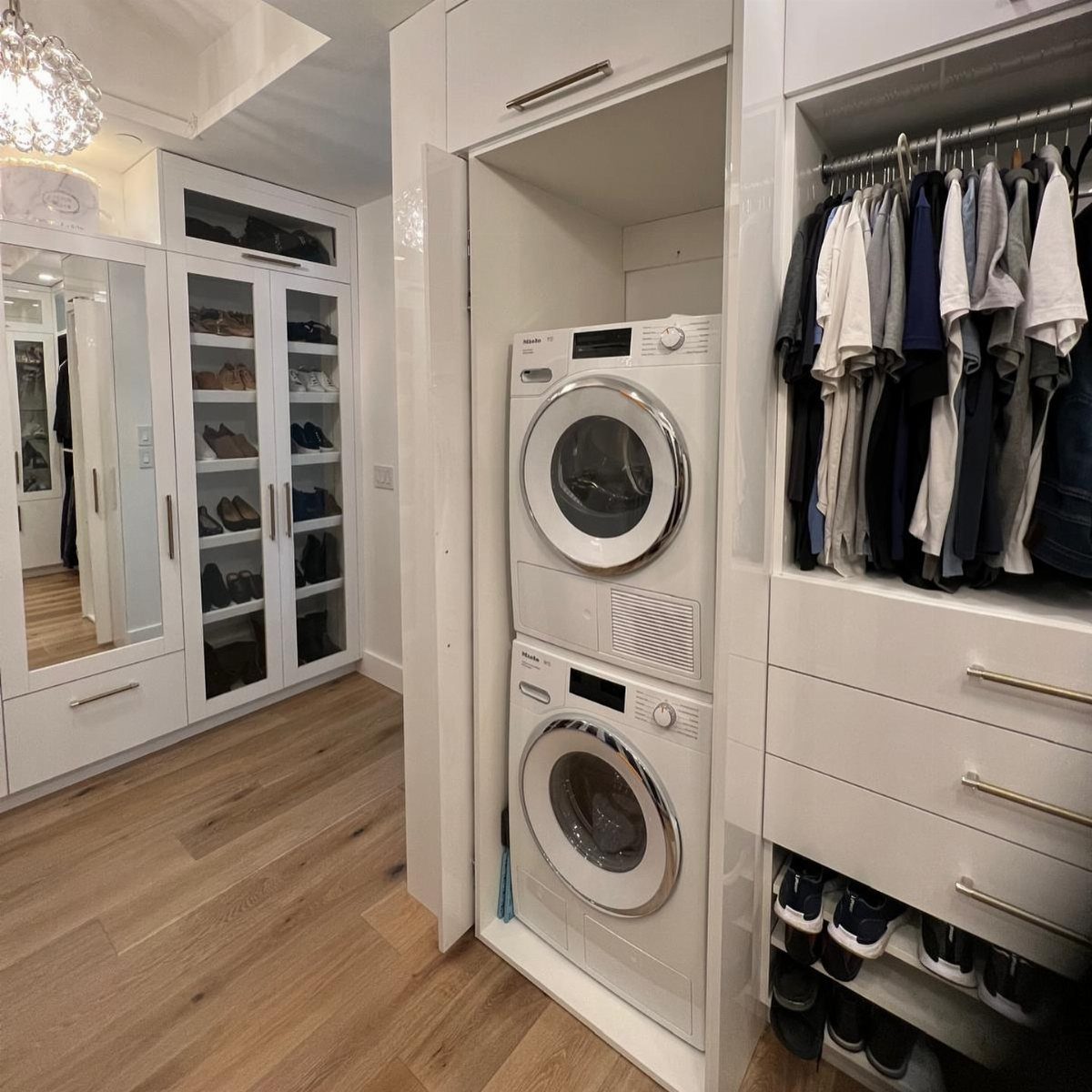 Stacked white washer and dryer integrated into custom white closet cabinetry with open doors.