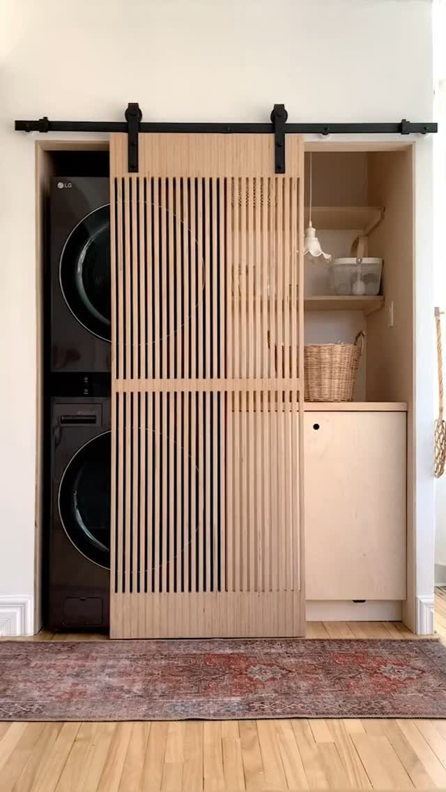 Slatted wood sliding barn door partially concealing a stacked washer and dryer unit.