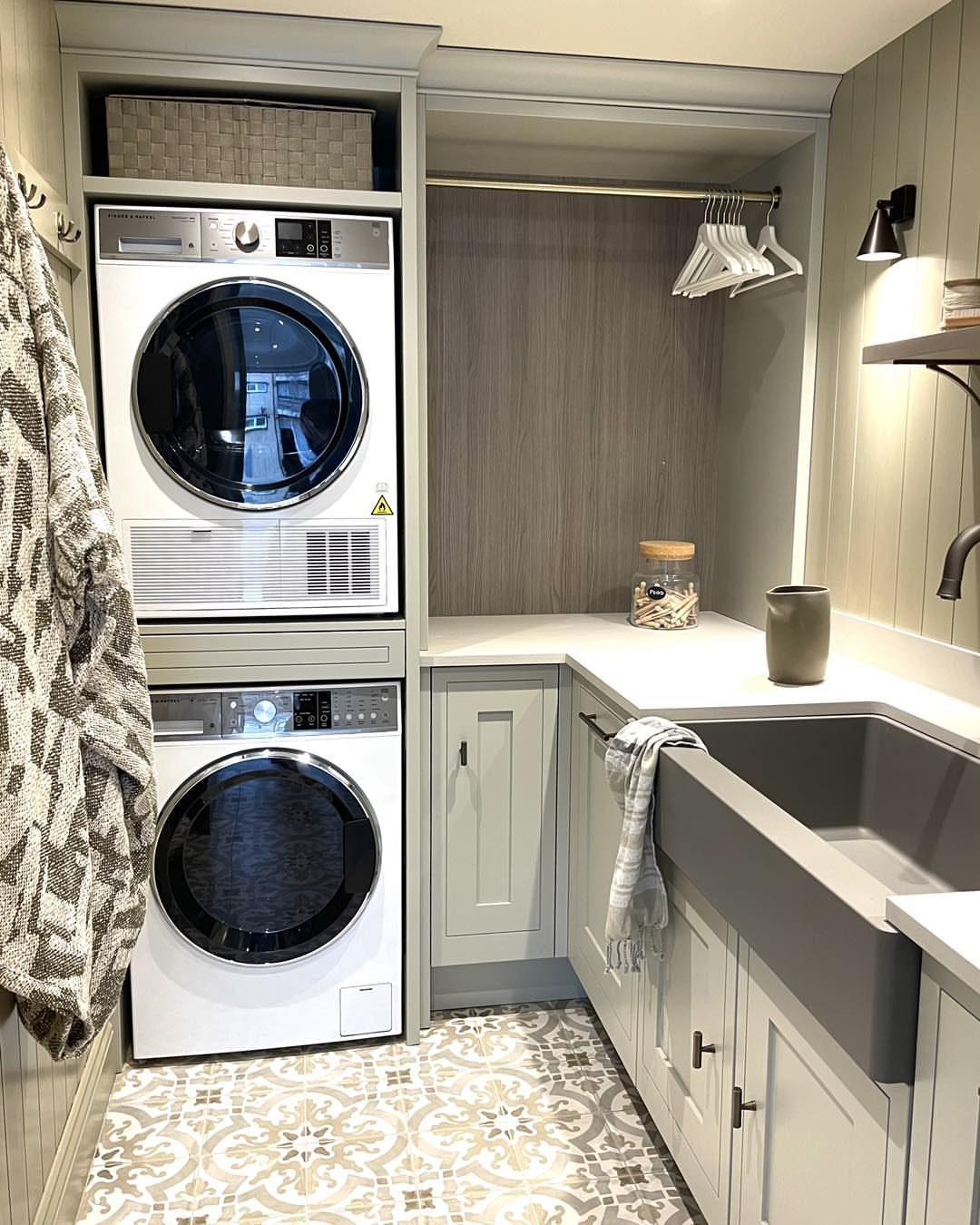 Stacked white washer and dryer in a grey laundry closet with farmhouse sink.