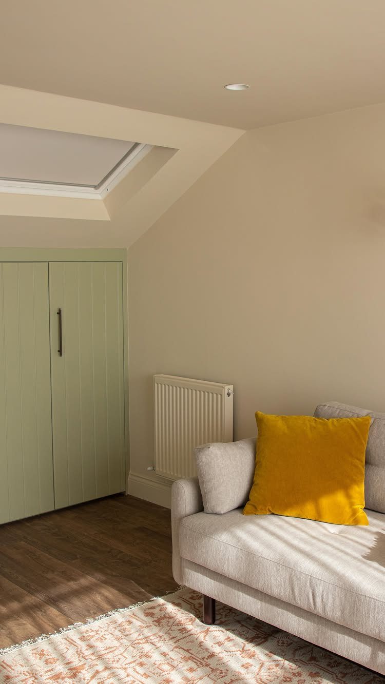 Light green wardrobe and grey sofa in a room with a slanted ceiling.