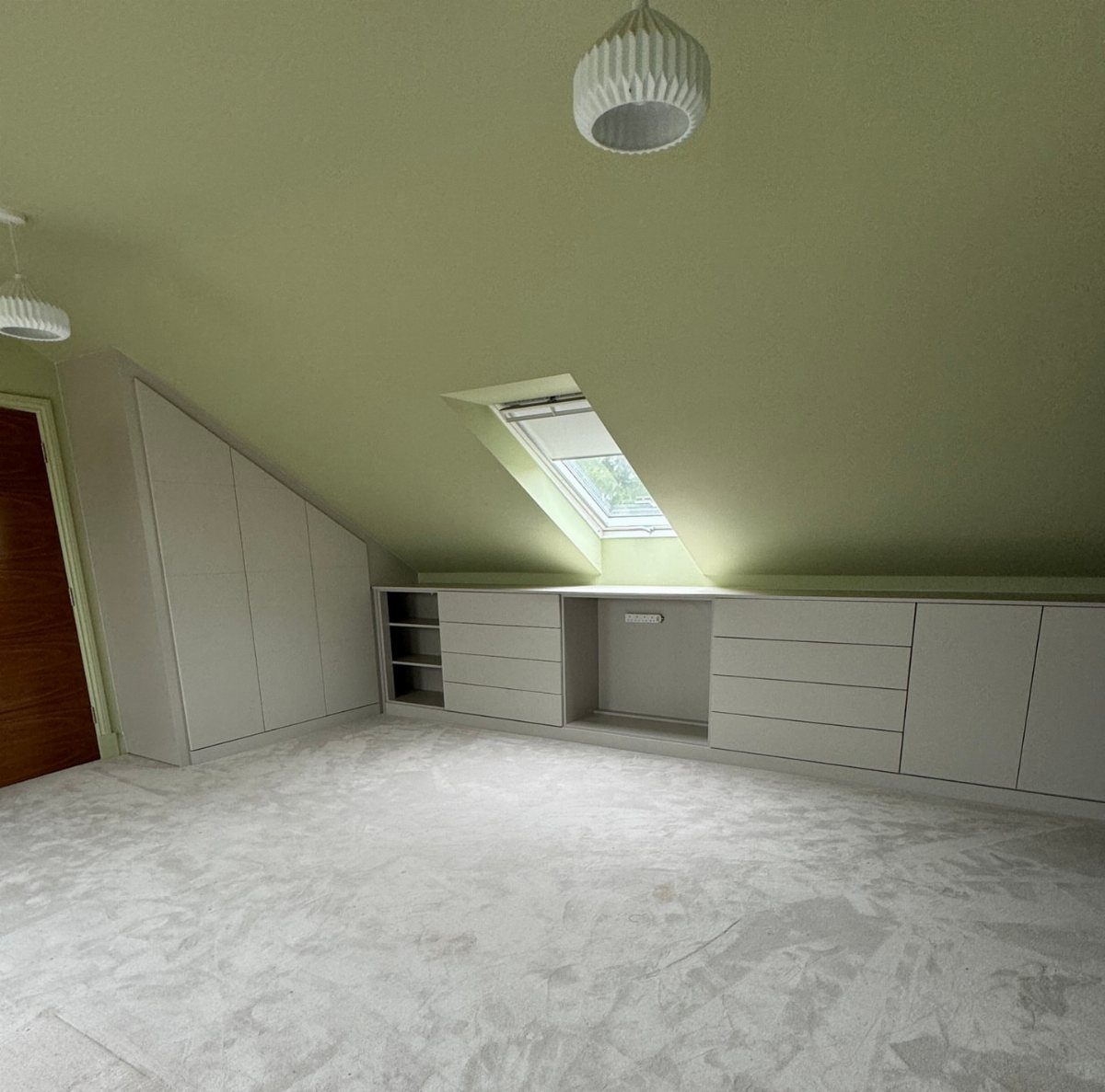 White built-in cabinets and drawers installed under a slanted light green ceiling.