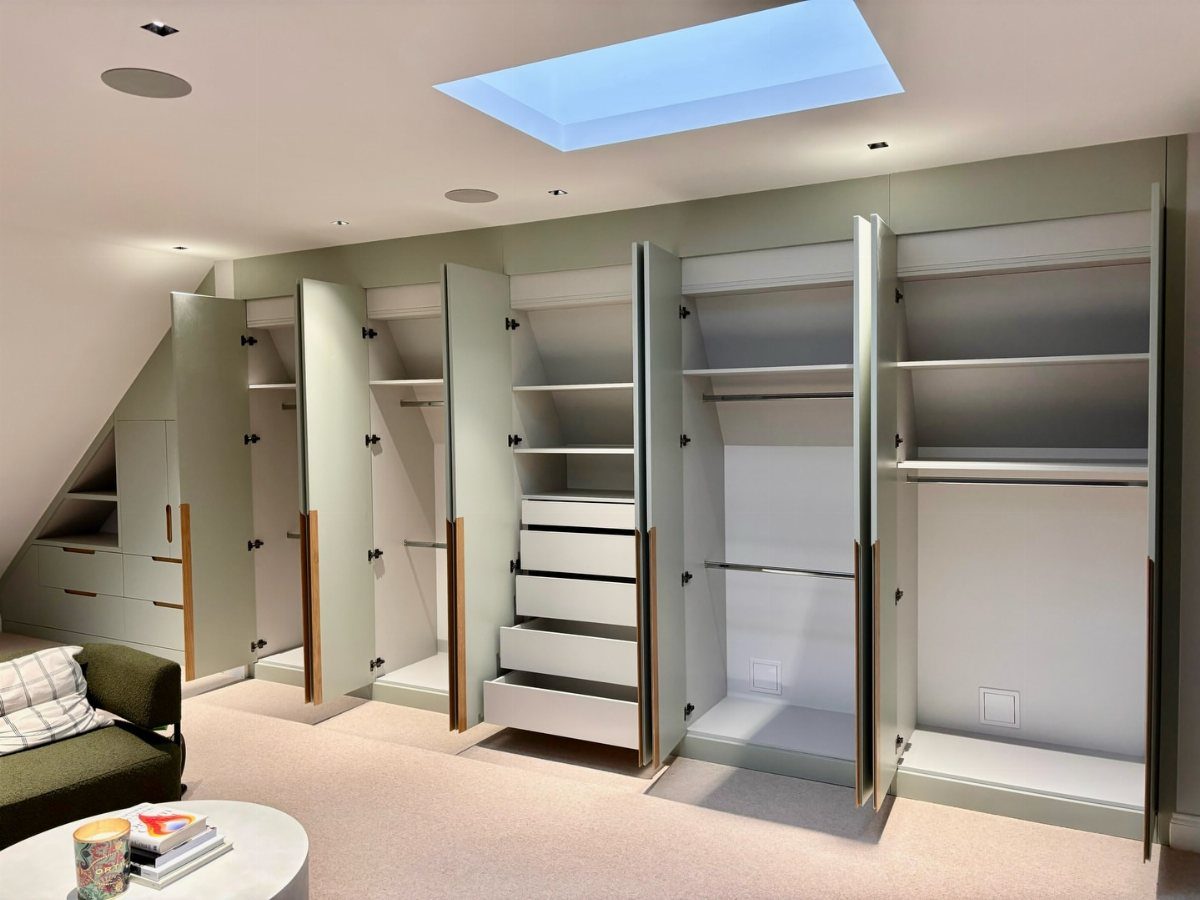 Modern walk-in closet with light green cabinets under a slanted ceiling and skylight.