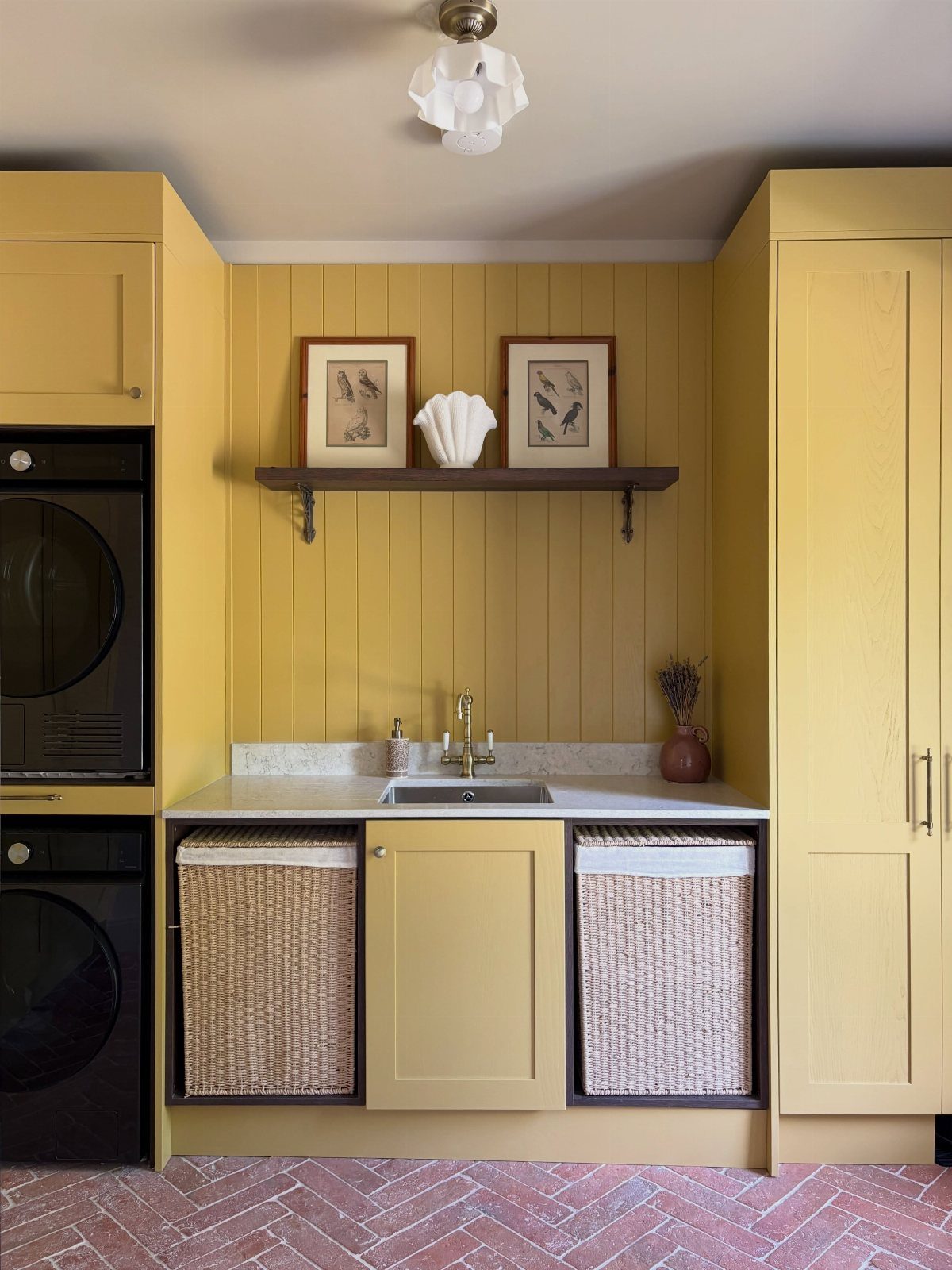 Yellow laundry room with woven baskets, a small sink, and red brick flooring.