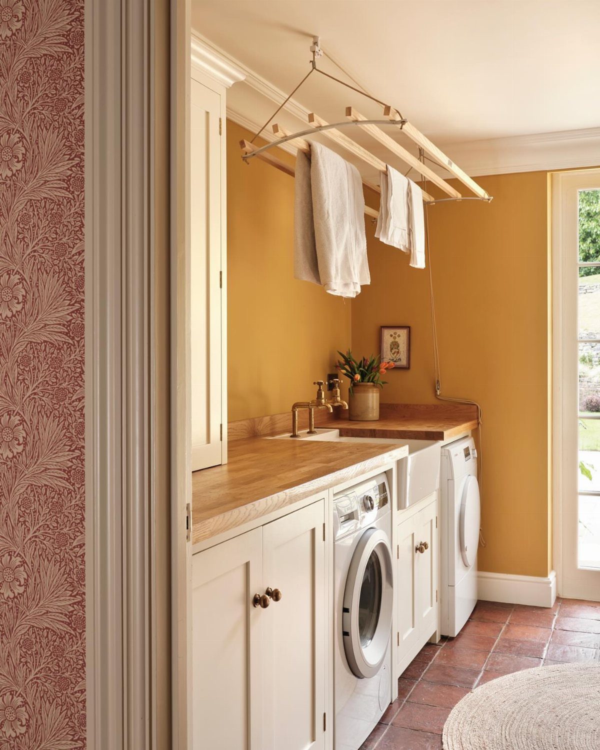 Laundry room with mustard yellow walls, white cabinets, and a ceiling drying rack.