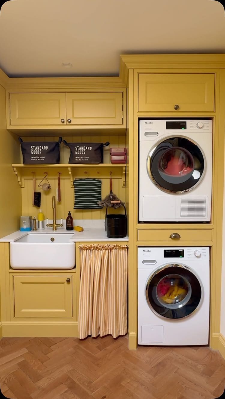 Pale yellow laundry room with stacked white machines and a farmhouse sink.