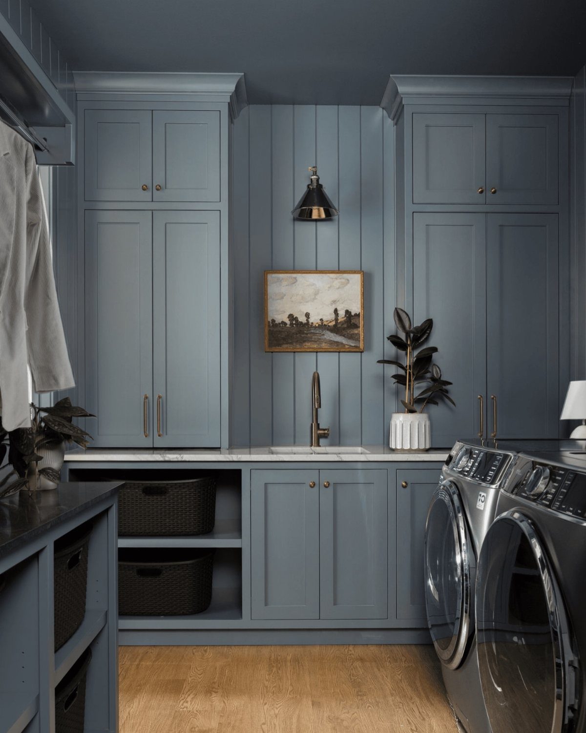 Blue-grey laundry room cabinets with a white countertop and modern washing machines.
