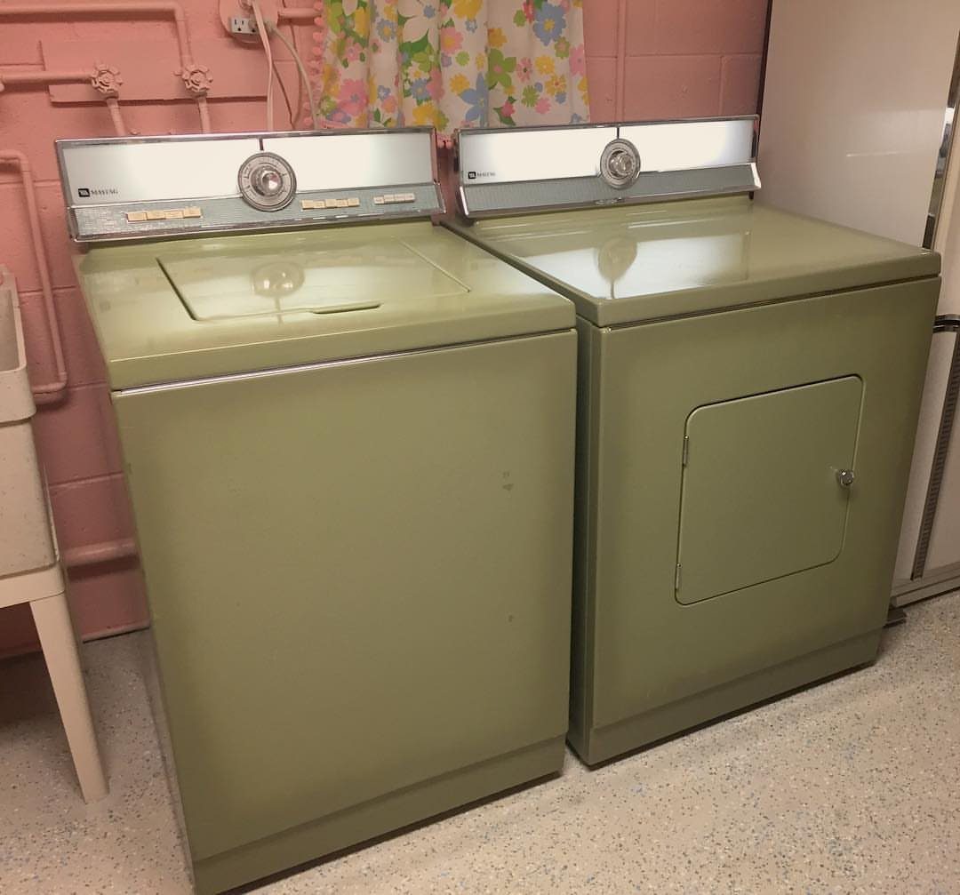Vintage olive green washer and dryer set against a pink wall with floral curtains.