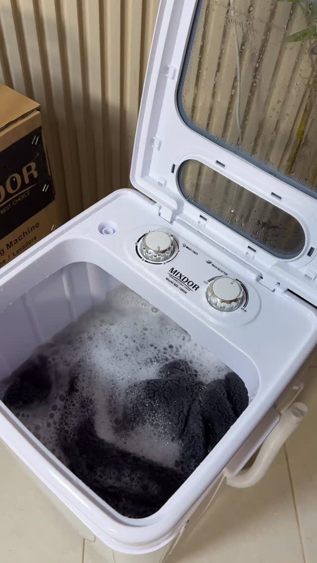 Compact white washing machine with open lid filled with soapy dark laundry