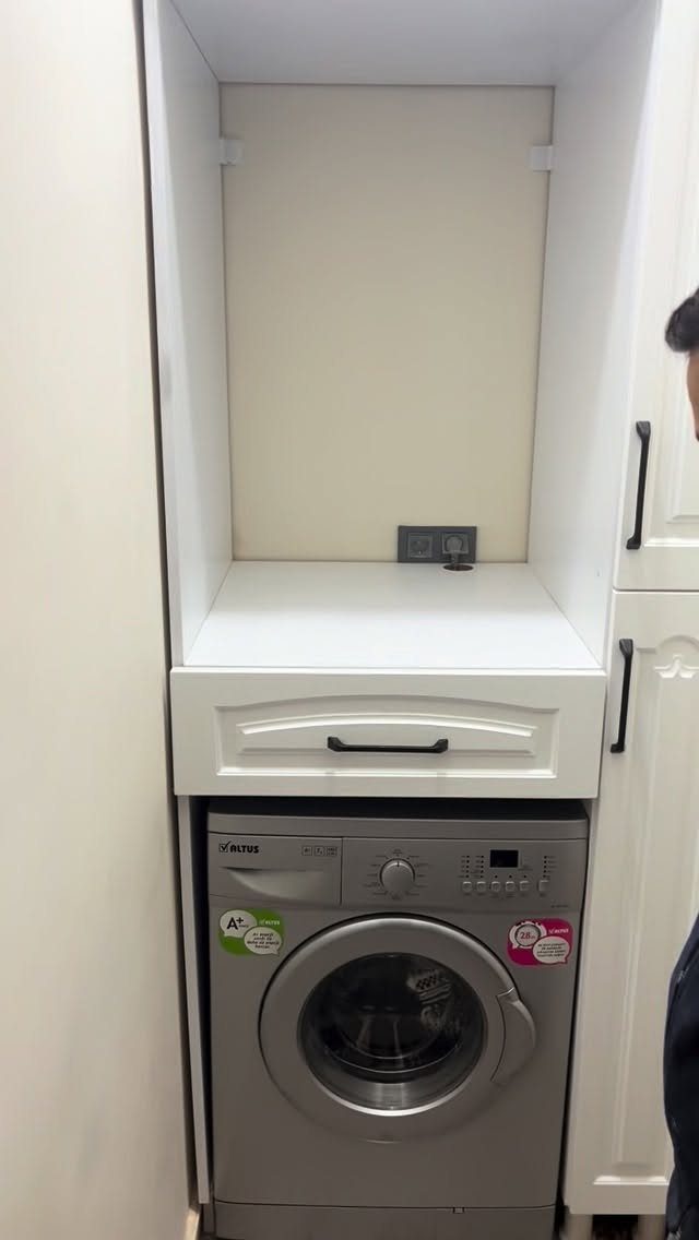 Silver front-loading washing machine installed inside a white built-in laundry cabinet
