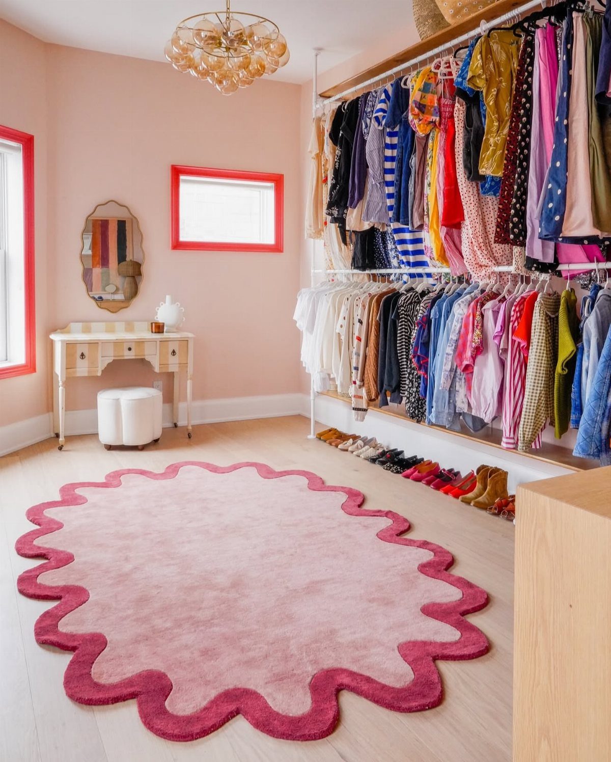Pink scalloped rug on light wood floor in a contemporary walk-in closet.