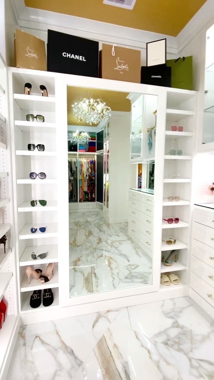 White walk-in closet with open shelving displaying sunglasses and luxury shopping bags.