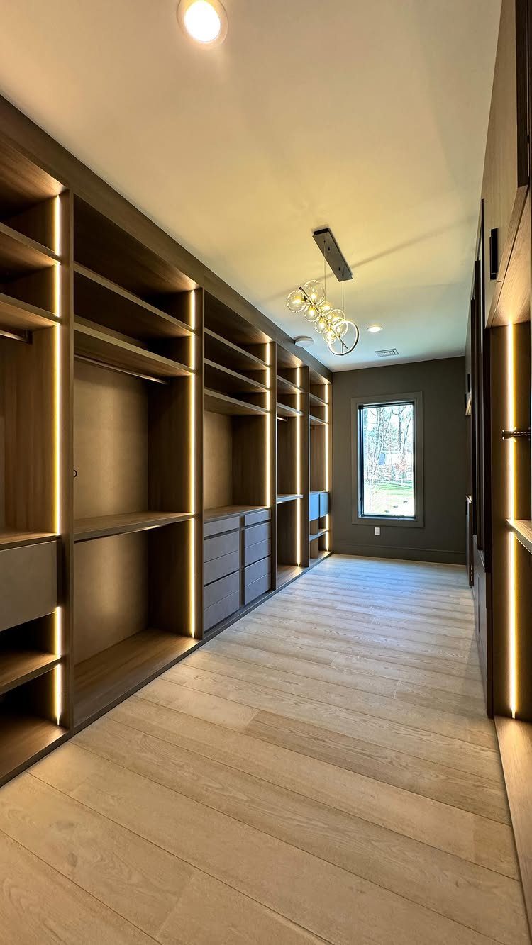 Dark wood walk-in closet with integrated LED lighting and light hardwood floors.