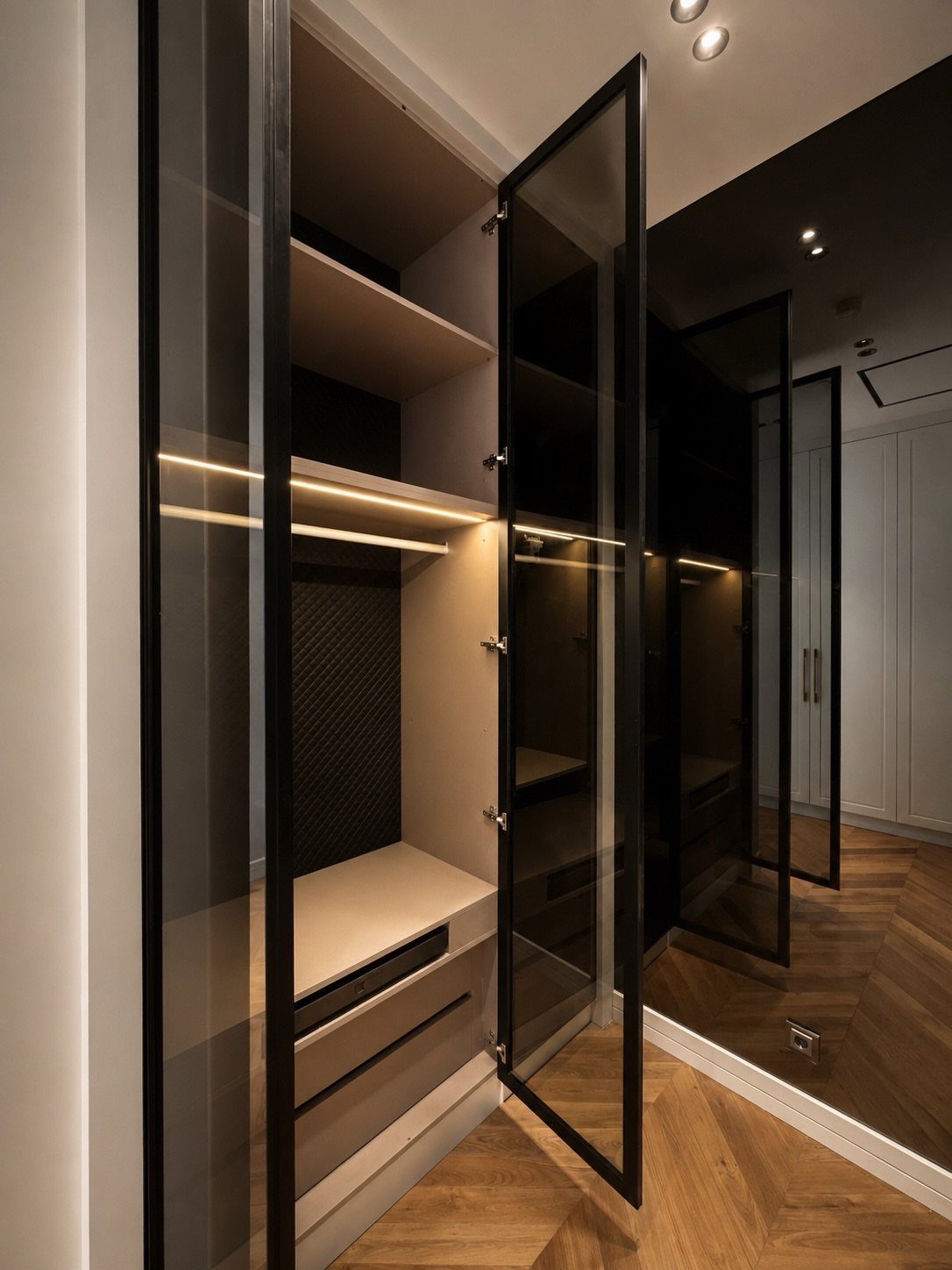Modern walk-in closet with black-framed glass doors and integrated LED shelf lighting.