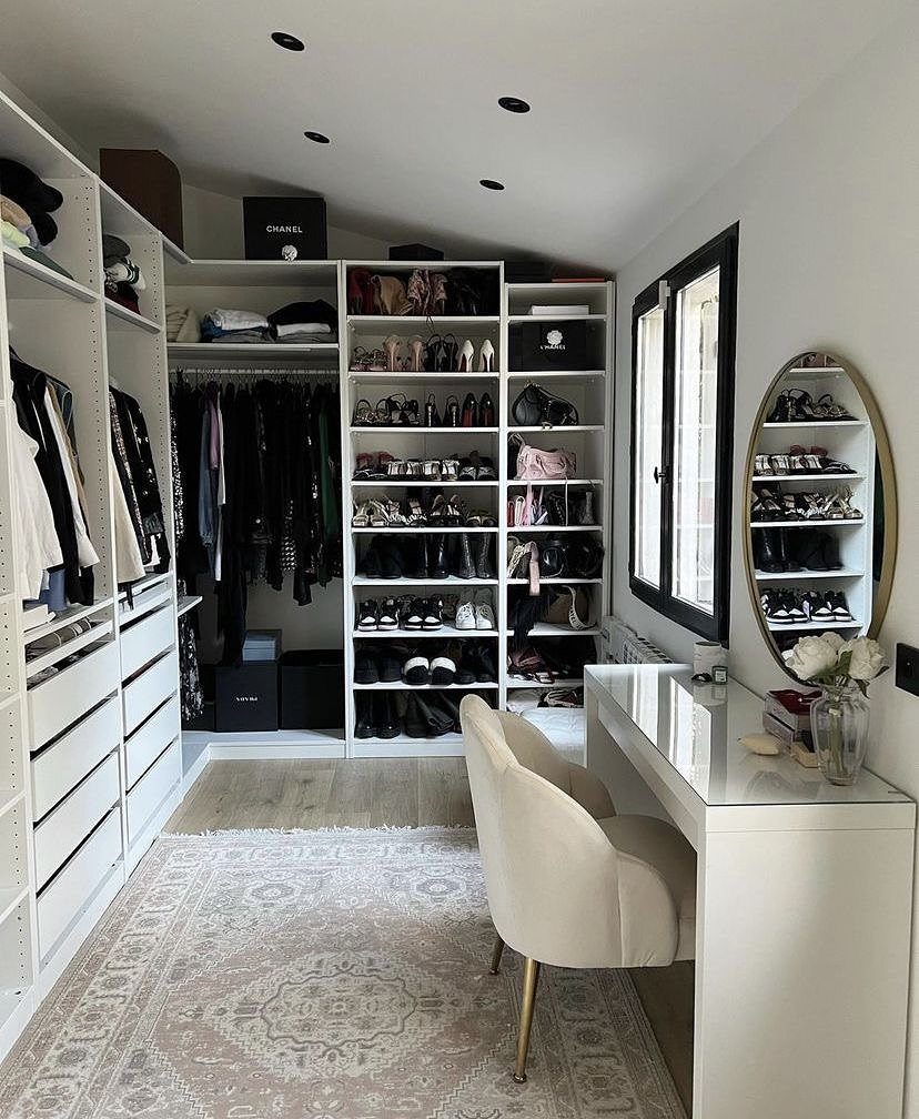 White walk-in closet with a vanity area, shoe shelves, and a light rug.