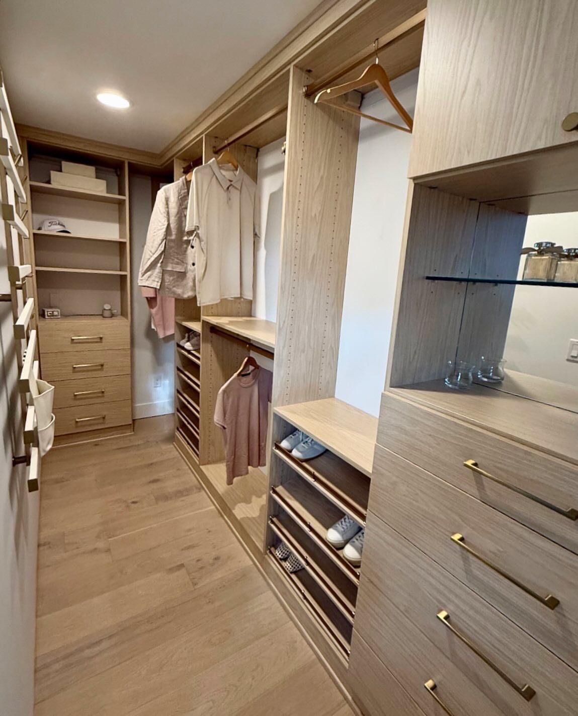 Light wood narrow walk-in closet with built-in drawers, hanging rods, and shoe shelving.