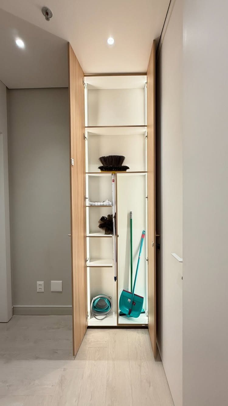 Narrow white closet with shelves and a tall compartment for cleaning supplies.