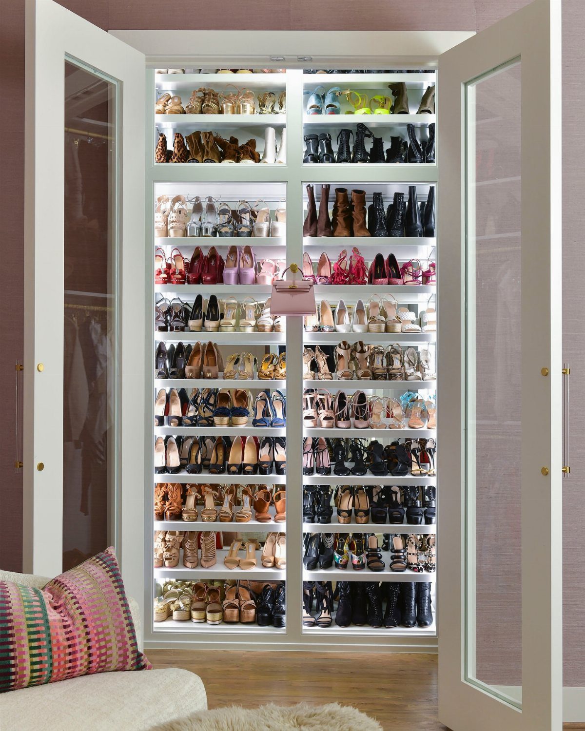 Deep narrow closet with white shelves filled with organized colorful shoes and boots.