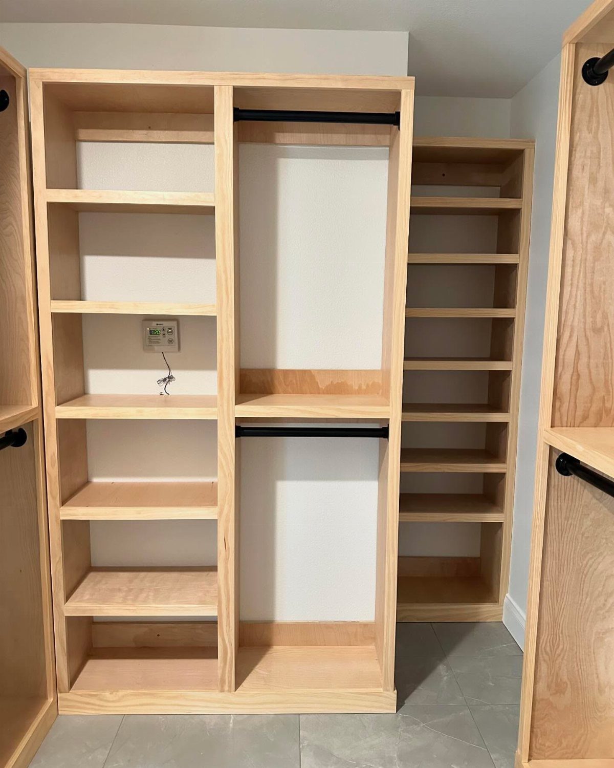 Wooden closet organizer with built-in shelves and black hanging rods in a room.