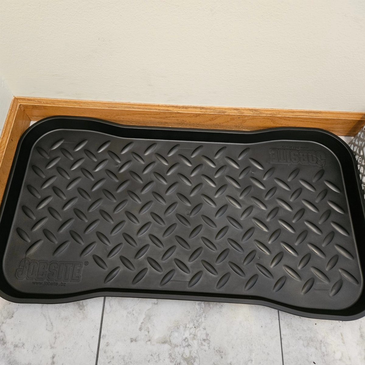 Black plastic boot tray with diamond texture on a white marble floor.