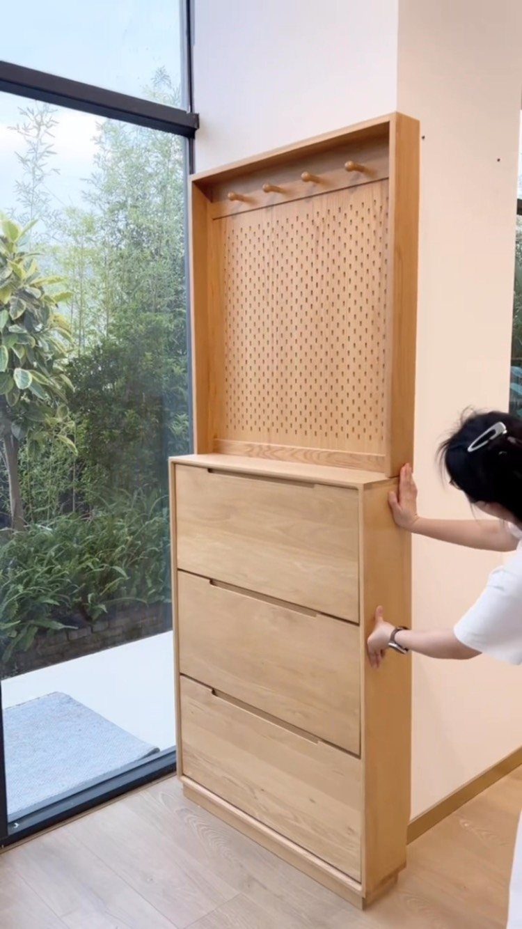 Wooden shoe storage unit with drawers and pegboard next to a glass door