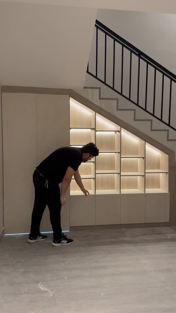 Built-in under-stairs storage unit with illuminated shelves and a man standing beside it.