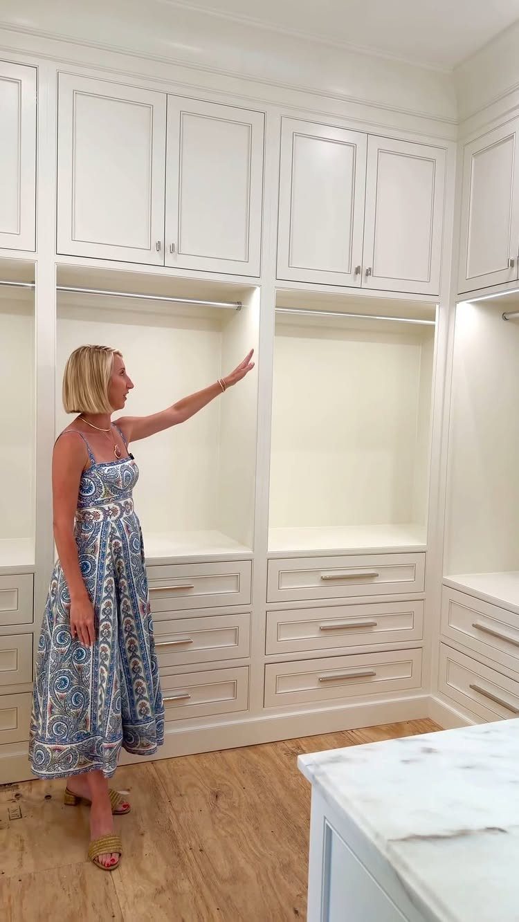 Woman standing in a white walk-in closet with matching cabinets and silver hardware.