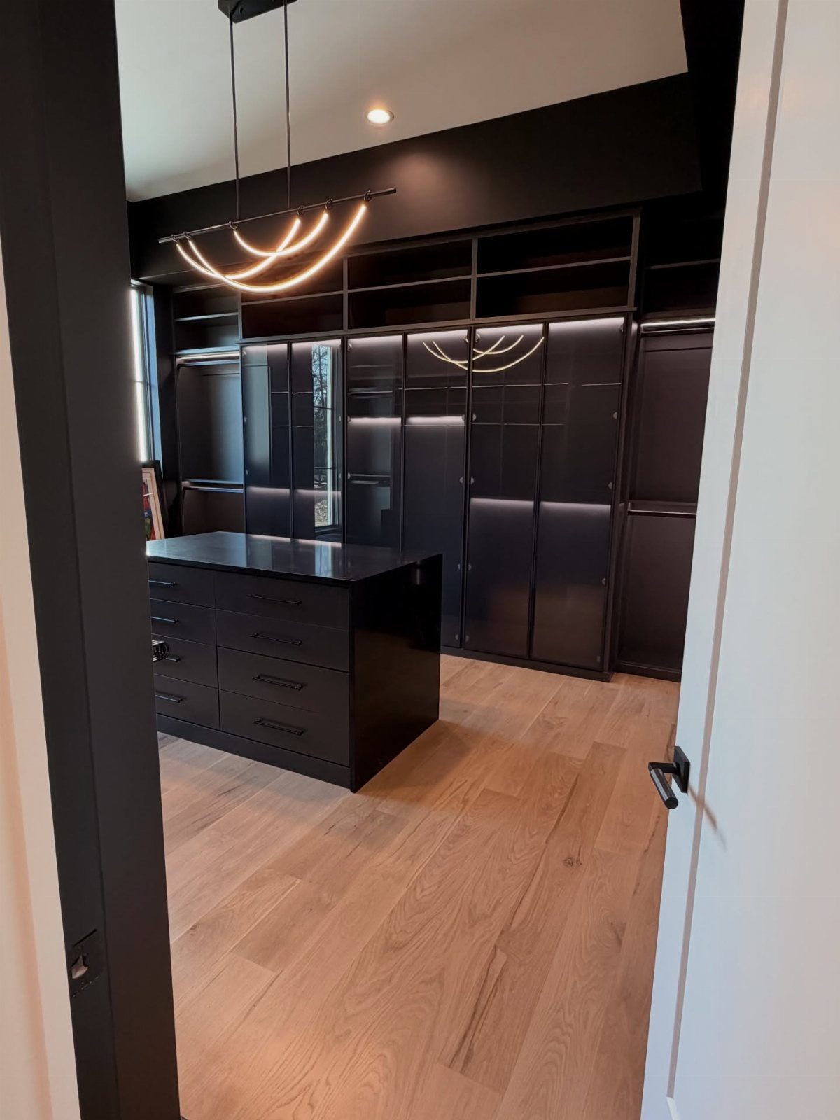 Modern black walk-in closet featuring a gold pendant light and integrated LED shelving.