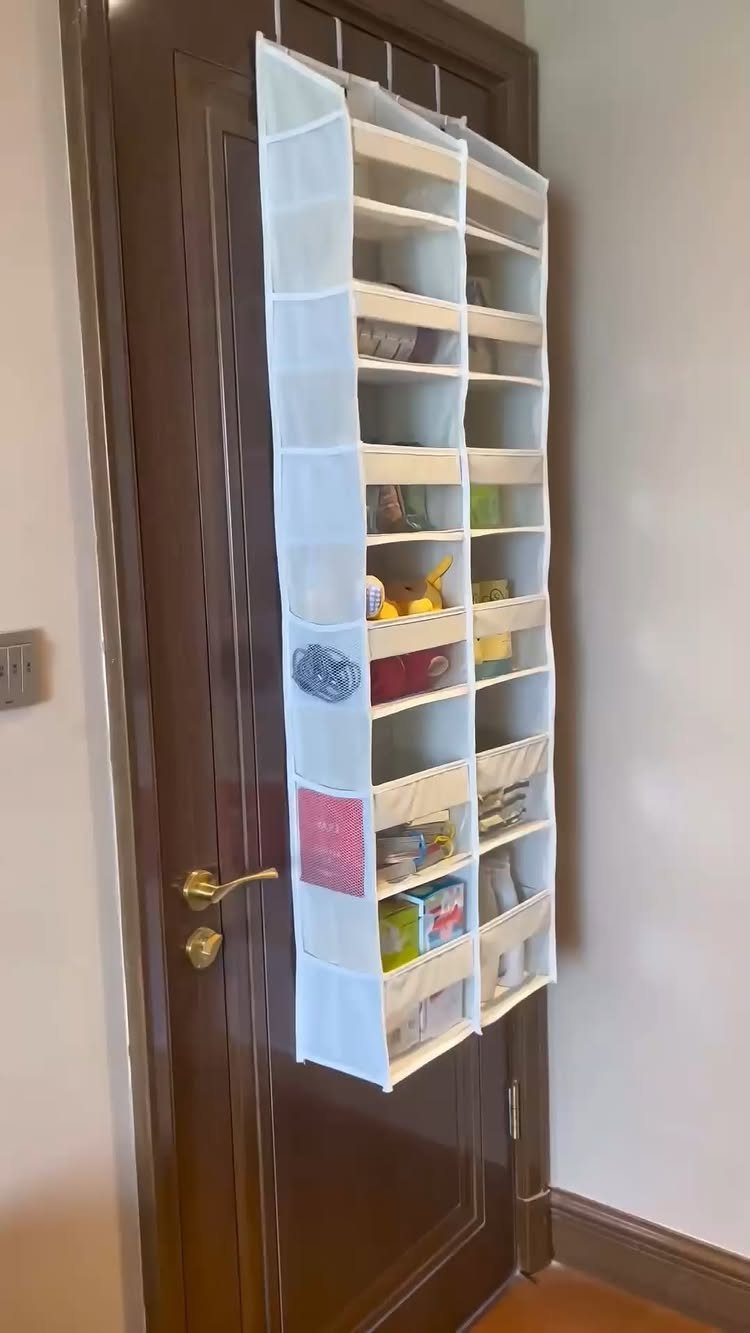 White fabric hanging organizer with pockets suspended from a dark brown wooden door