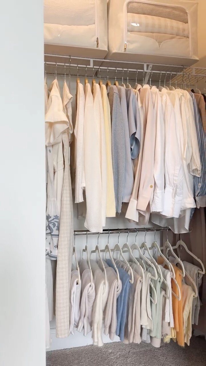 Light-colored clothes hanging on two rods with fabric storage bins on top shelf