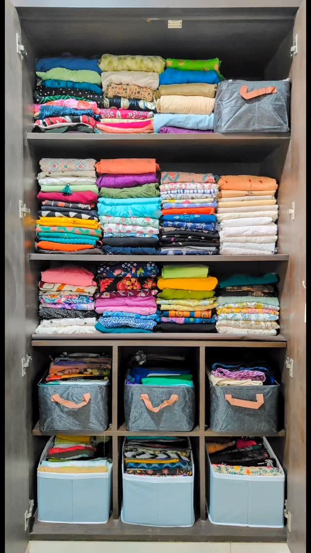 Folded colorful clothes stacked on wooden shelves with fabric storage bins below.