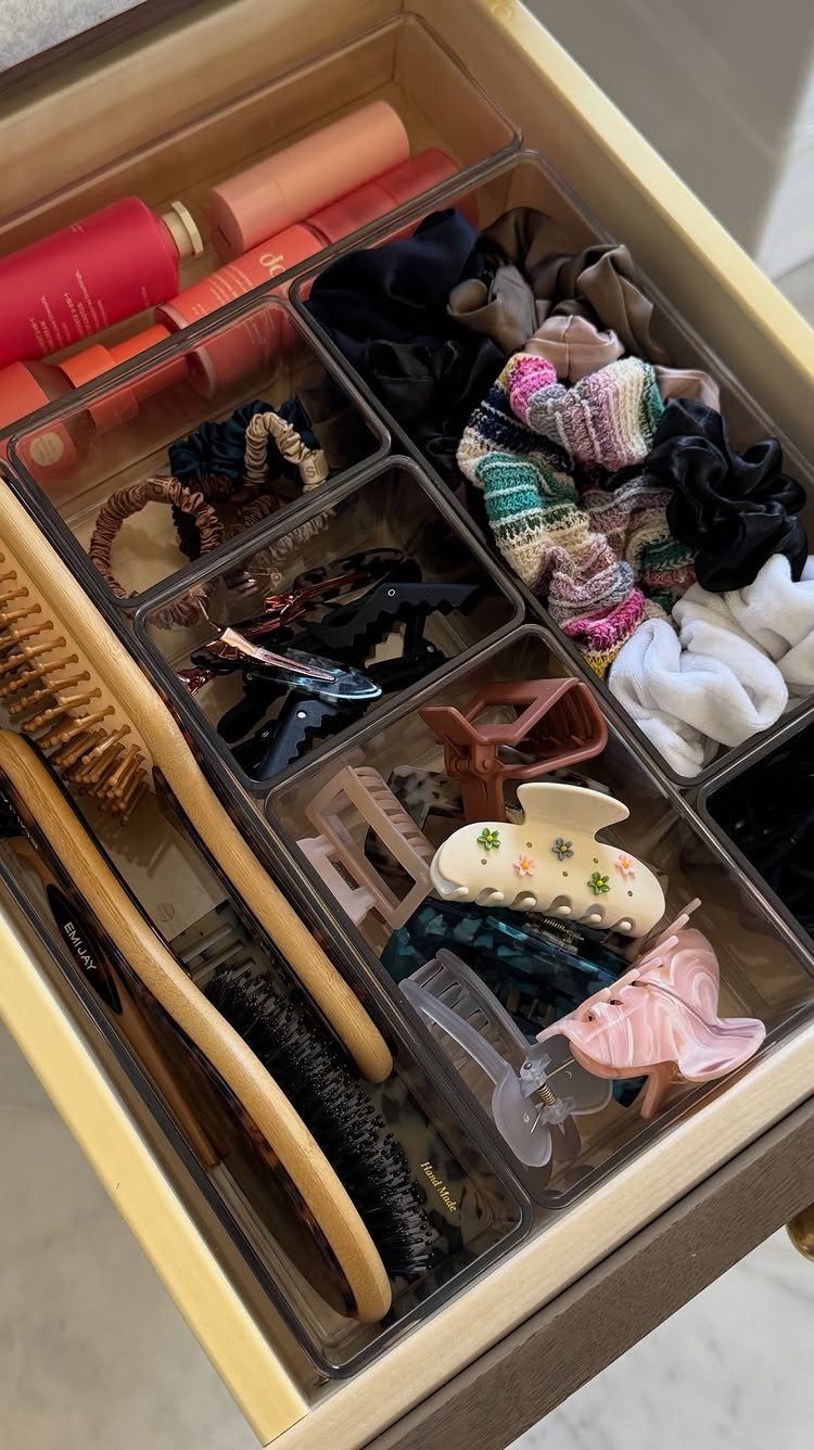 Clear plastic drawer organizers holding hair accessories, brushes, and cosmetic tubes.