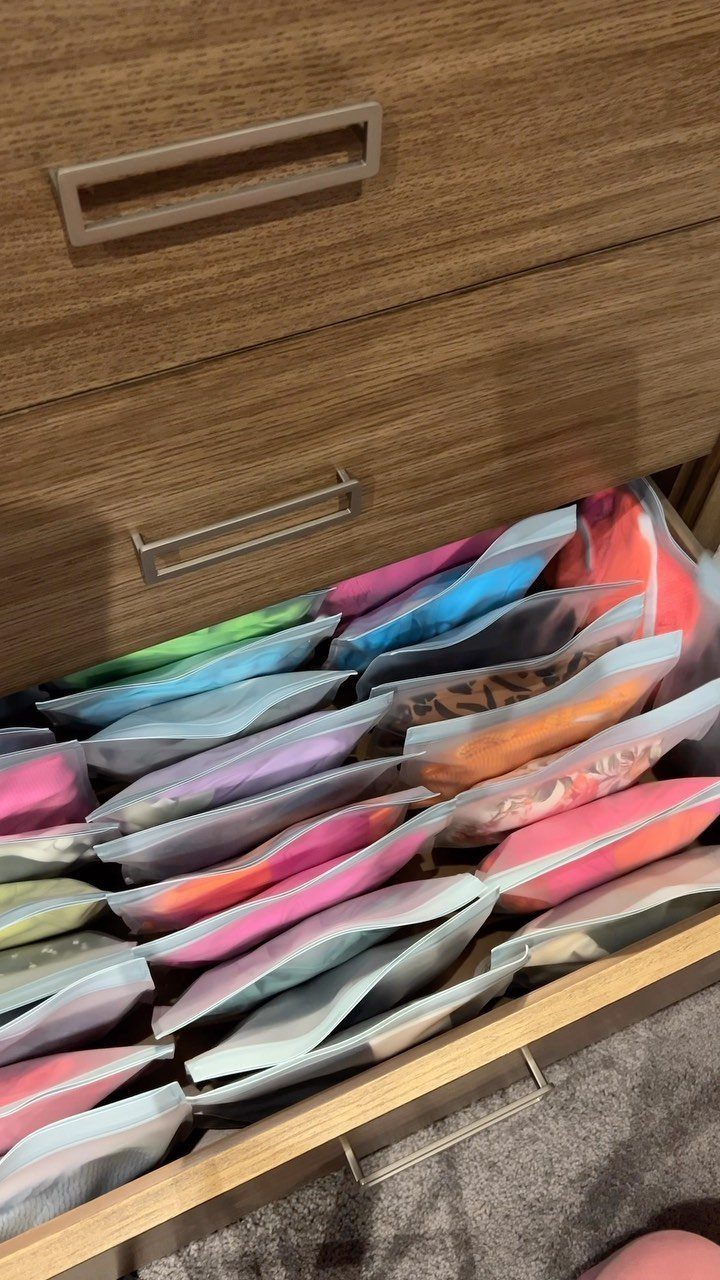Open wooden drawer containing colorful clothes stored in clear vacuum compression bags.