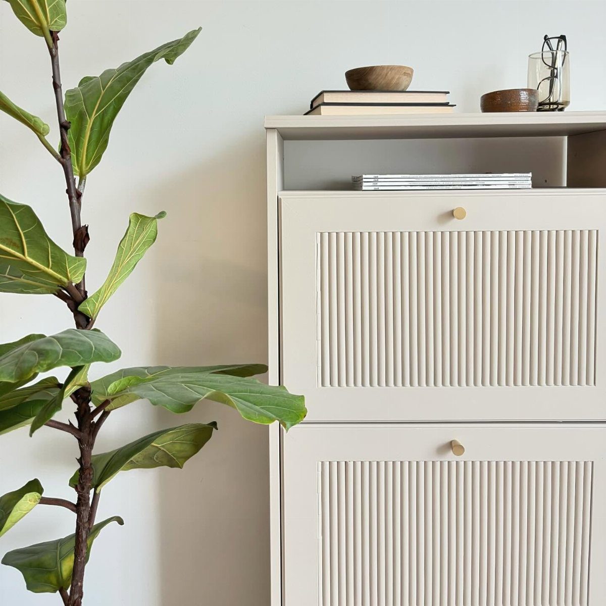 White fluted storage cabinet with gold knobs next to a fiddle leaf fig plant