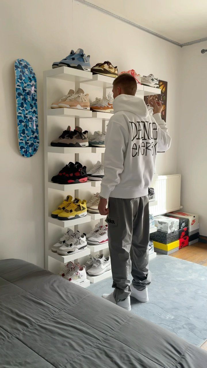 Man standing by white floating shelves displaying a collection of colorful sneakers