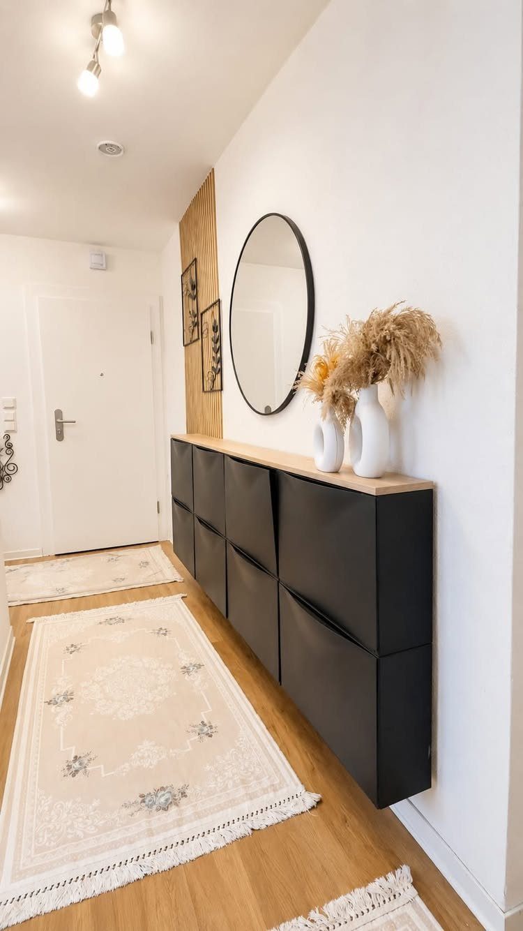 Black shoe cabinet with wooden top in a bright hallway with round mirror.