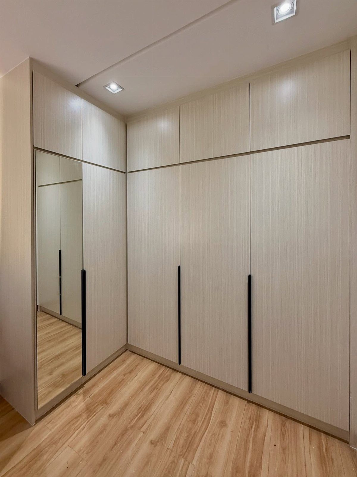 L-shaped walk-in closet with light wood cabinets and a full-length mirrored door.