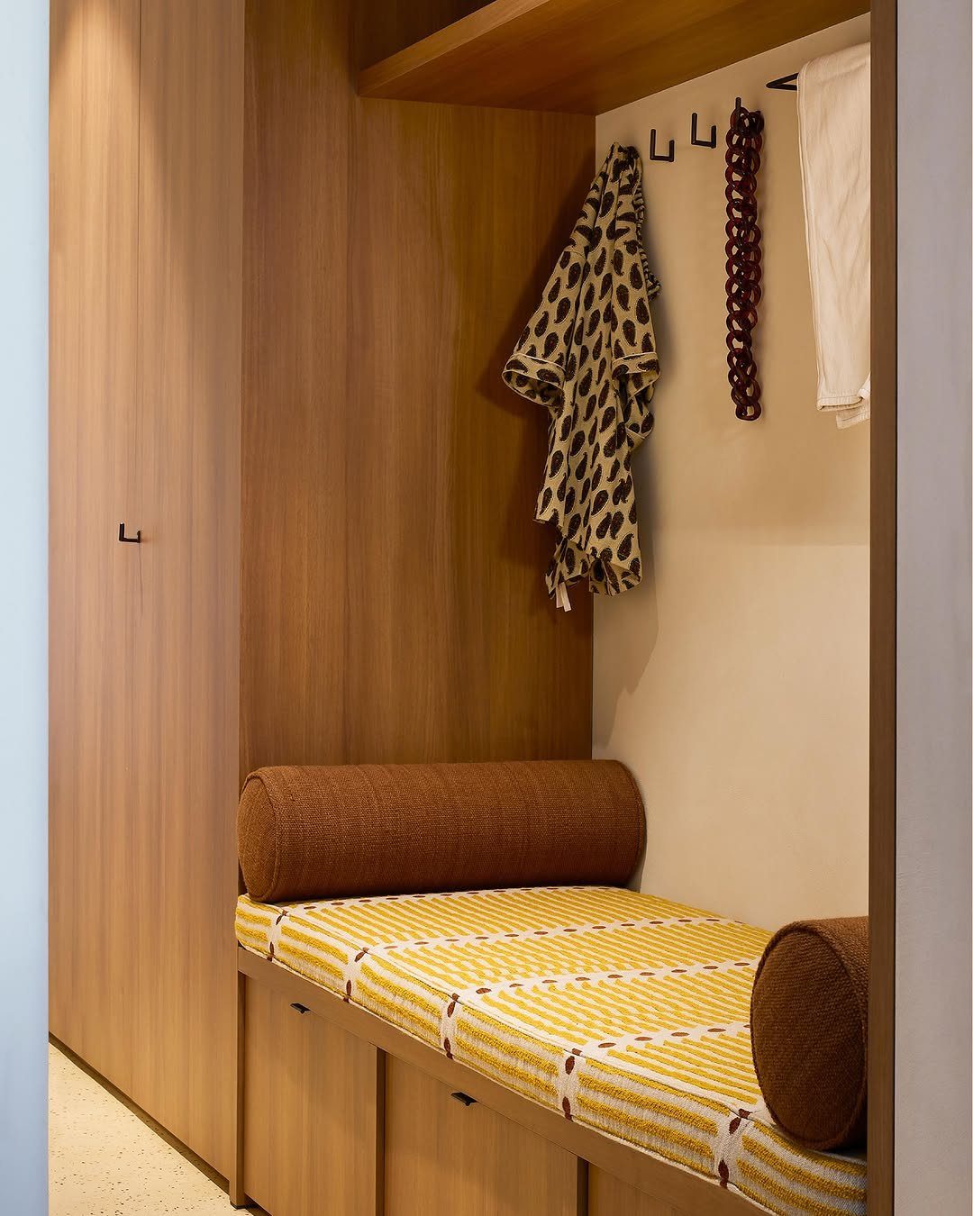 Wooden closet nook with a striped bench and black hooks holding accessories.