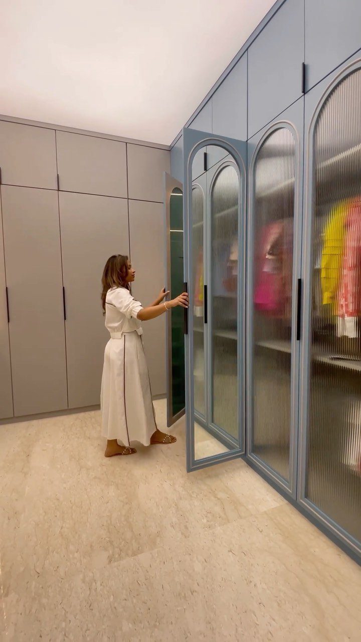 Woman standing in a large walk-in closet with blue fluted glass doors.
