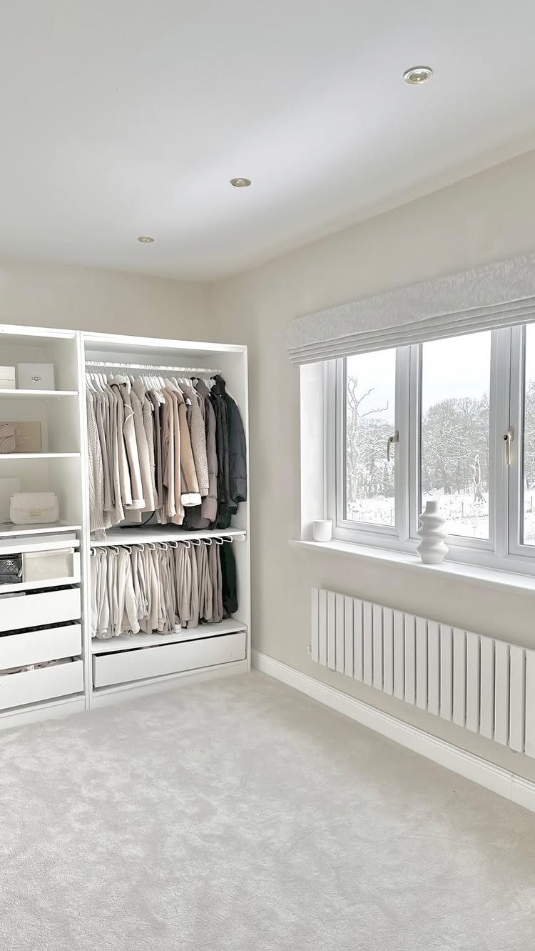 White walk-in closet with open shelving and hanging clothes next to a window.