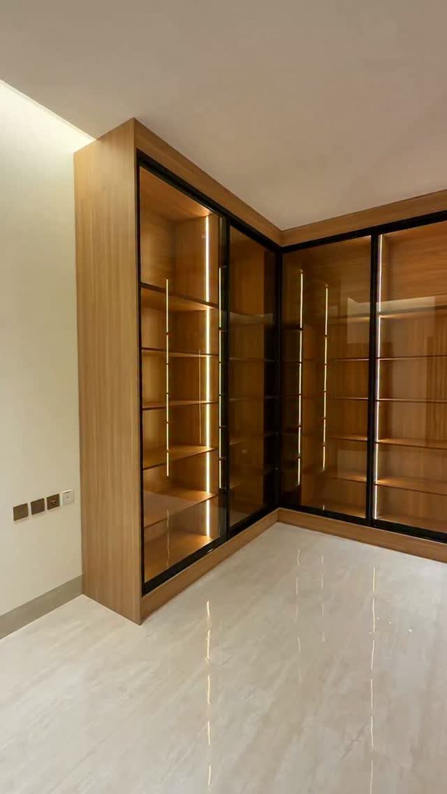 L-shaped walk-in closet with glass doors, wooden frames, and integrated LED lighting.