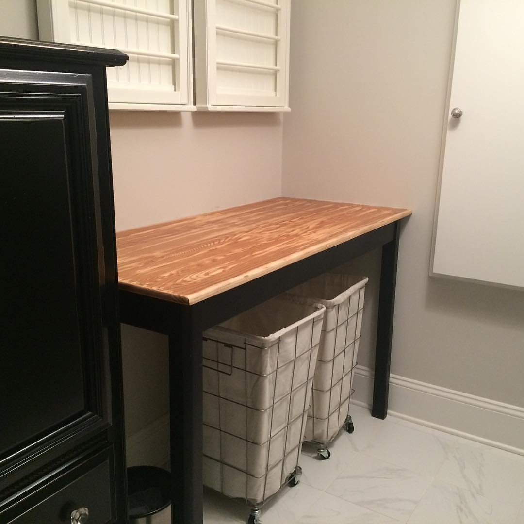 Wooden laundry folding table with two white rolling hampers stored underneath.