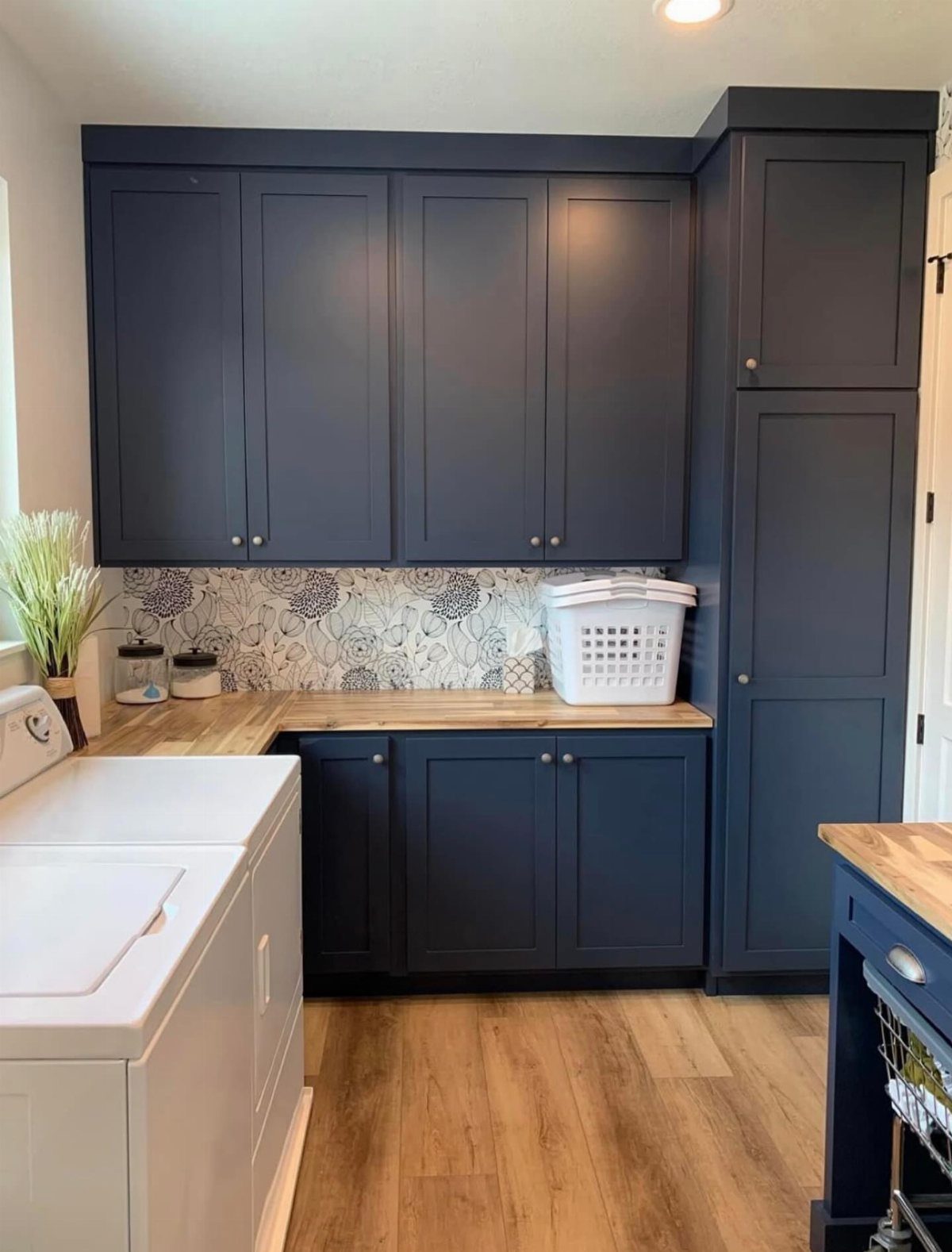Navy blue laundry cabinets with a light wood countertop and patterned backsplash.