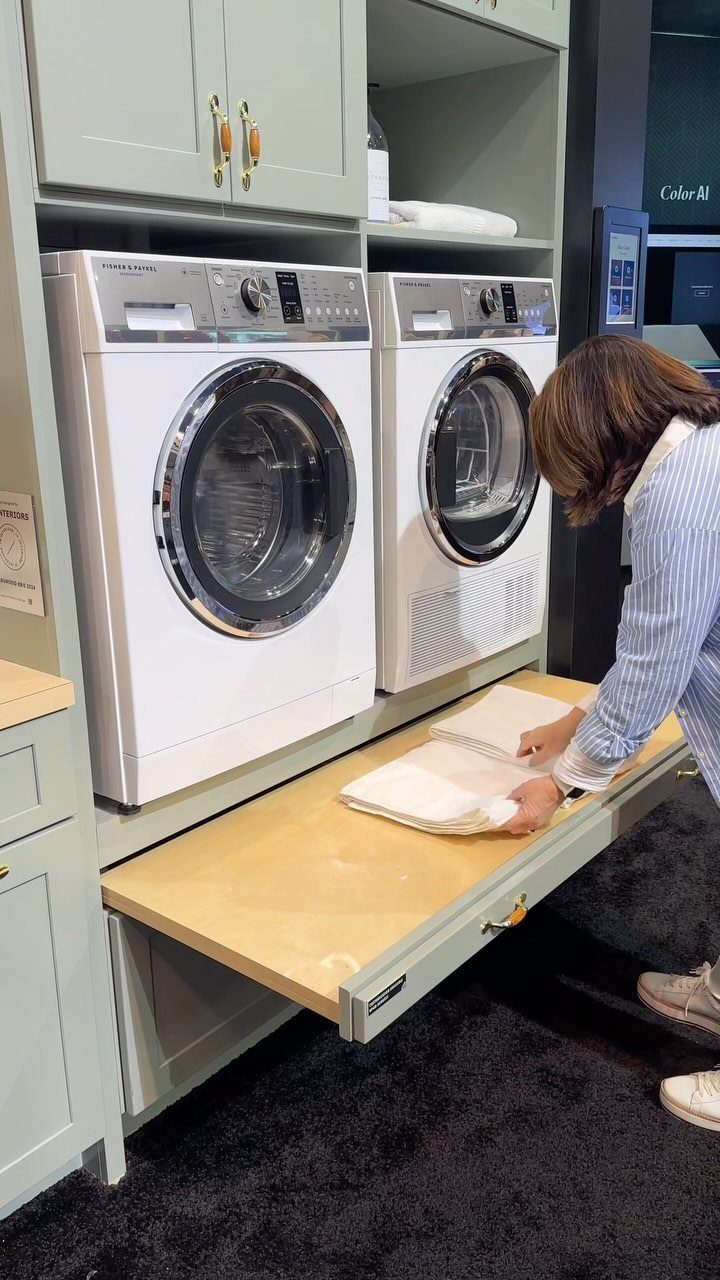 Person folding white towels on a wooden pull-out table in a laundry room.