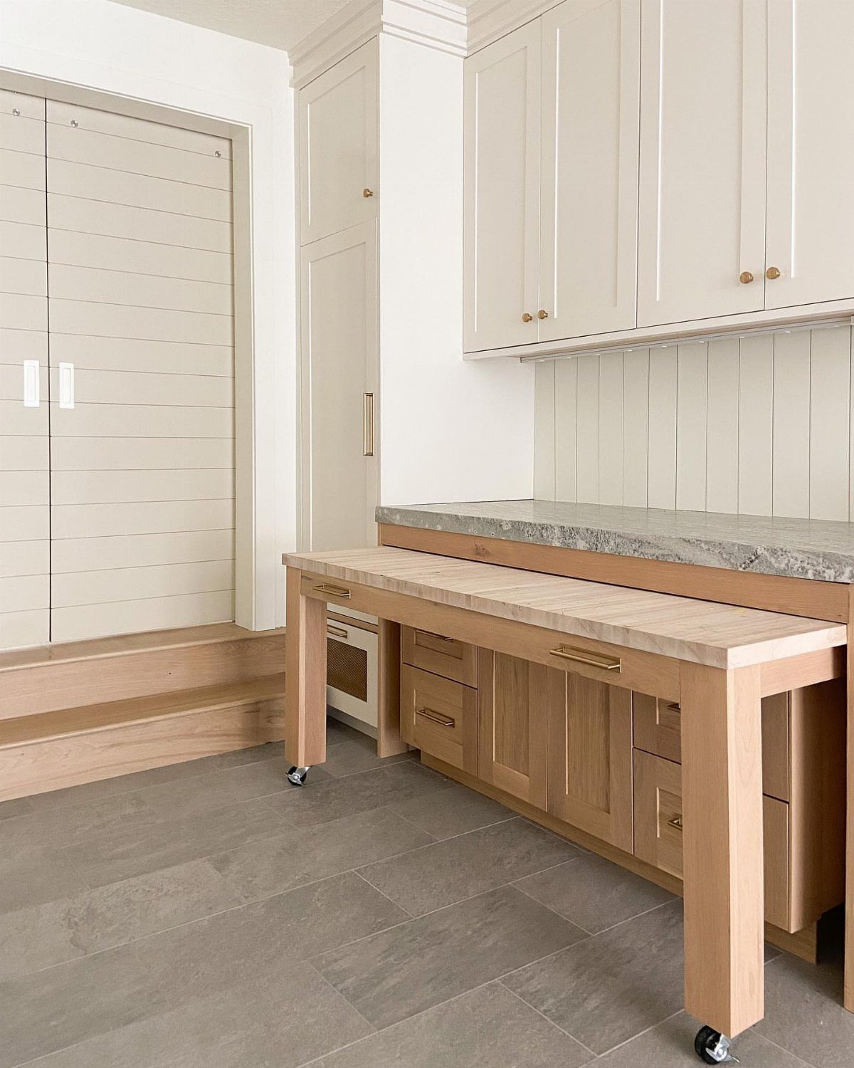 Rolling light wood laundry table with drawers in a white laundry room