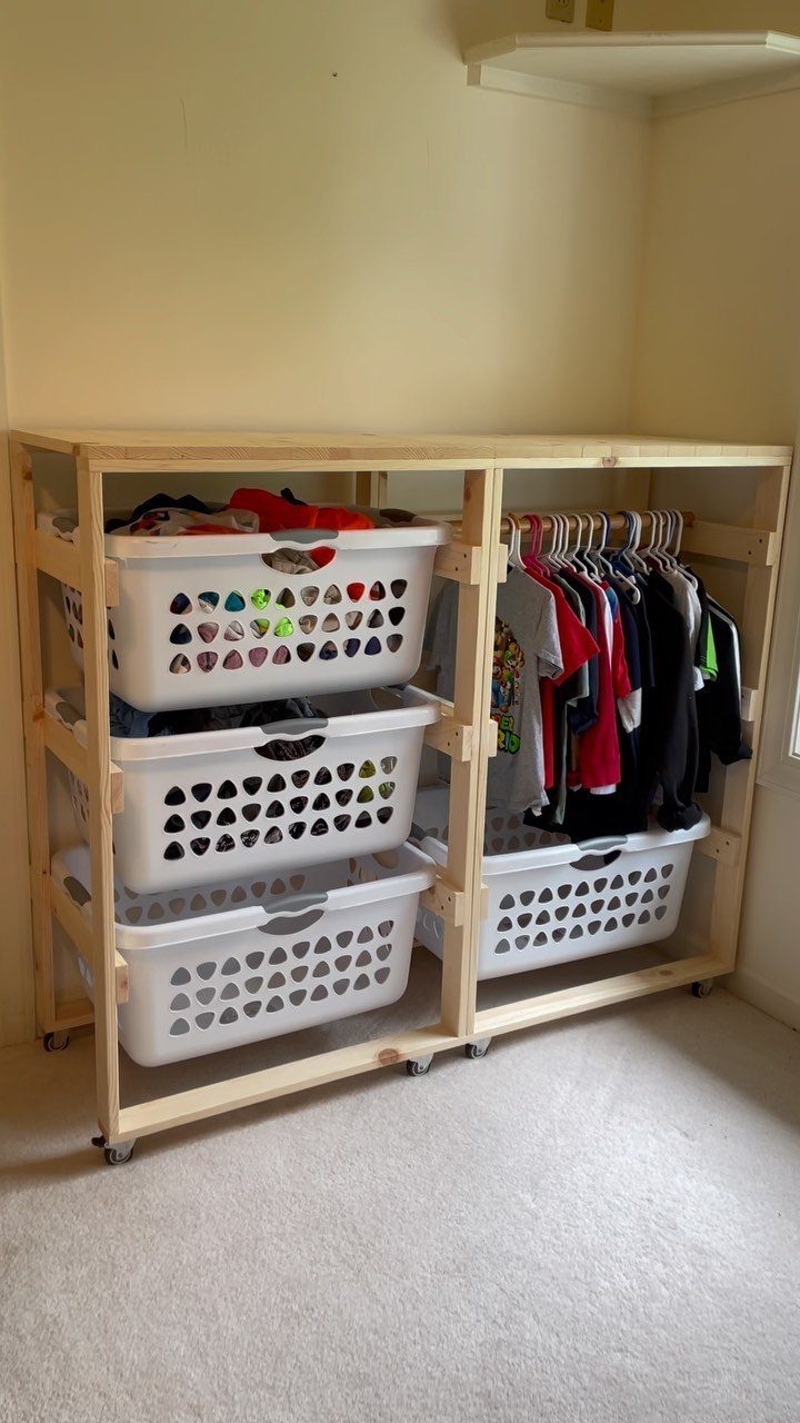 Wooden shelving unit with white laundry baskets and hanging clothes on a carpeted floor