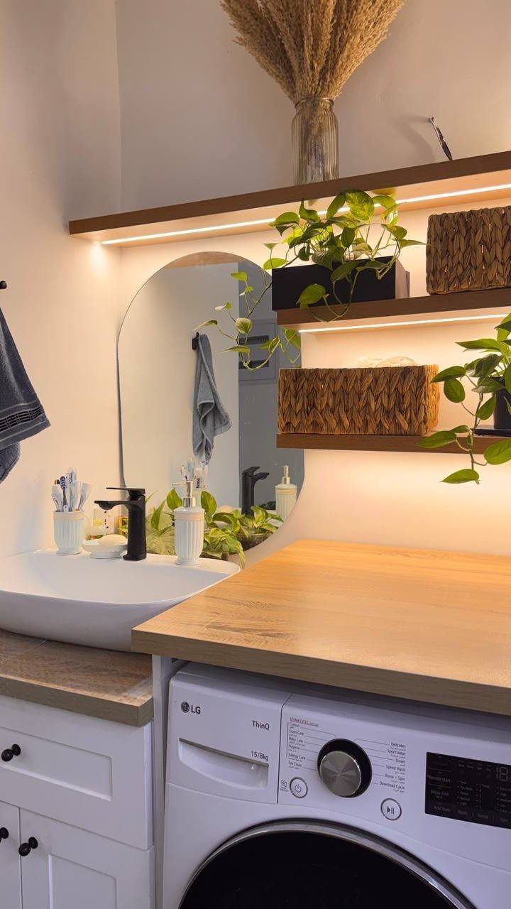Laundry room with integrated LED strip lighting under wooden floating shelves and plants.