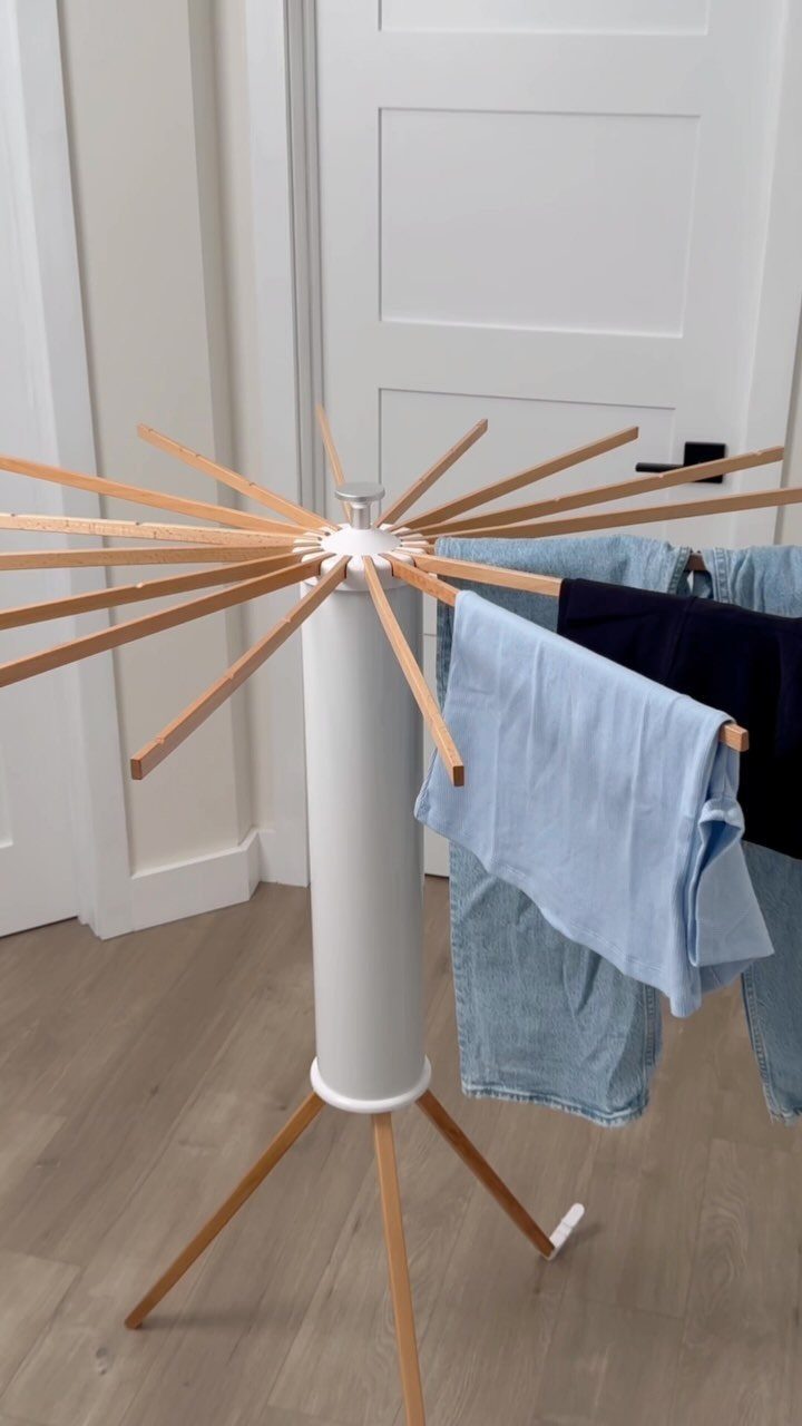White cylindrical drying rack with wooden spokes holding blue clothes in a room.