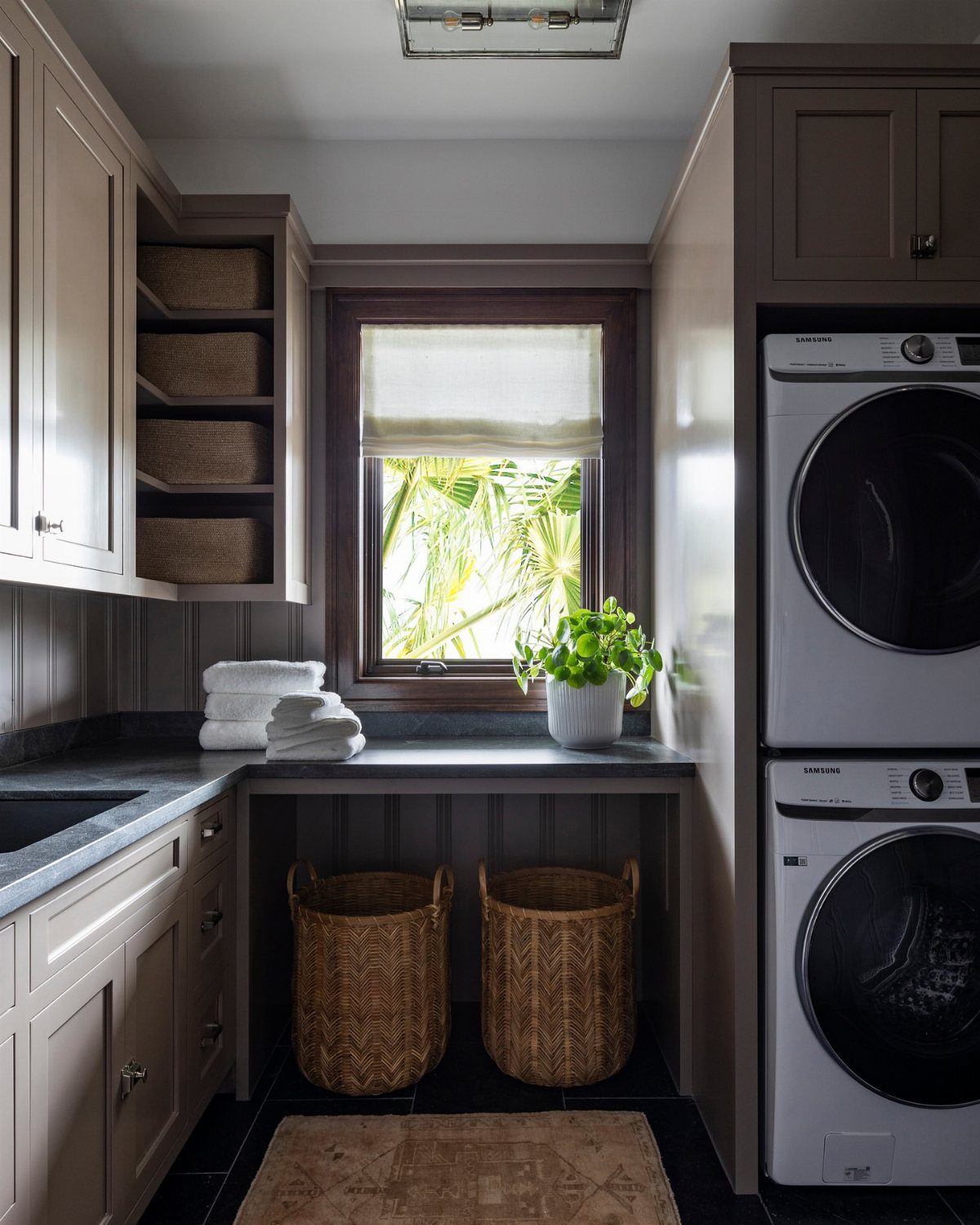 Laundry room with grey cabinets, stacked white washer and dryer, and woven baskets.